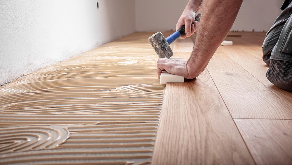 Handwerker verlegt Parkettboden und streicht den Estrich mit Kleber Bodenleger beim Verlegen des neuen Fußbodens